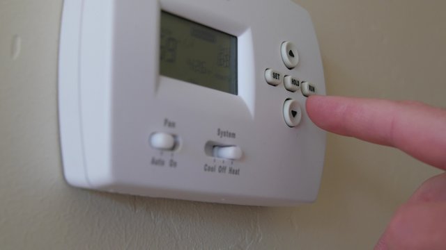 A finger programs the thermostat in a home