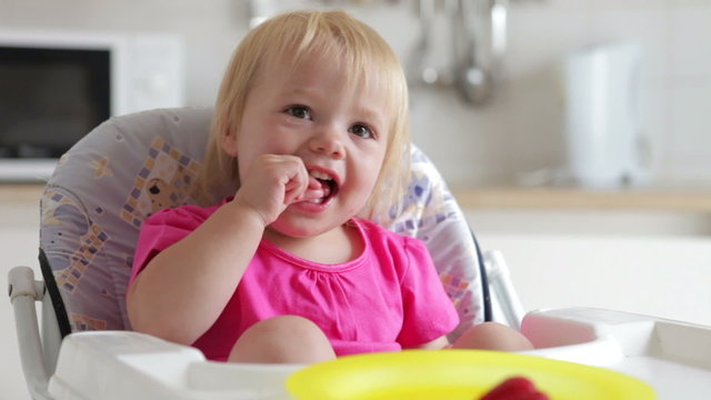 Young Girl Sitting In High Chair Eating Strawberry