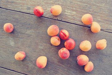 Fototapeta na wymiar Ripe fresh orange apricots scattered on the rustic wooden table. Image edited in faded, washed out, nostalgic, retro style; rural vintage concept. Organic farming concept.