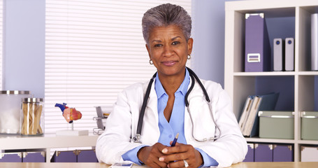 Senior African woman doctor sitting at desk and talking to camera