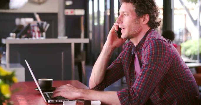 Man In Cafe Working On Laptop And Answering Phone