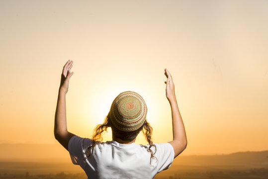 a jewish scholar raising arms at sunset