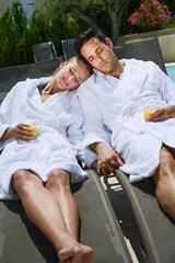beautiful young couple resting in deck chairs with bathrobe by the pool of a thalasso resort