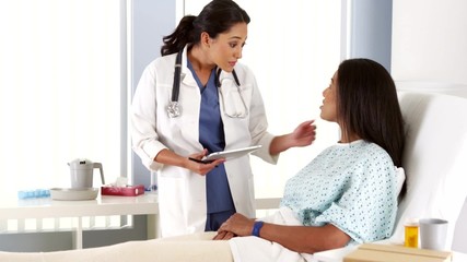 Female doctor talking to African American patient in hospital bed - Powered by Adobe