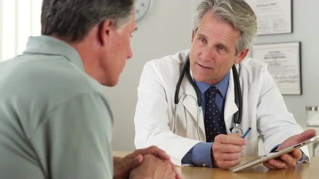 Senior doctor talking with patient and tablet in office