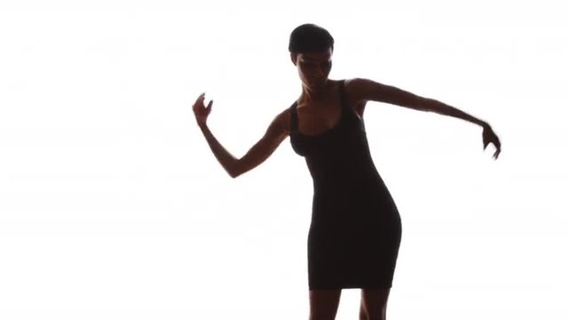 Woman in black dress smiling and dancing on white background in slow motion