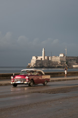 Brightly colored Cuban taxi drives in front of el Morro lighhouse along the Malecon in Central Havana.