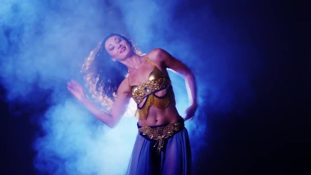 Sexy woman belly dancing in studio with fog