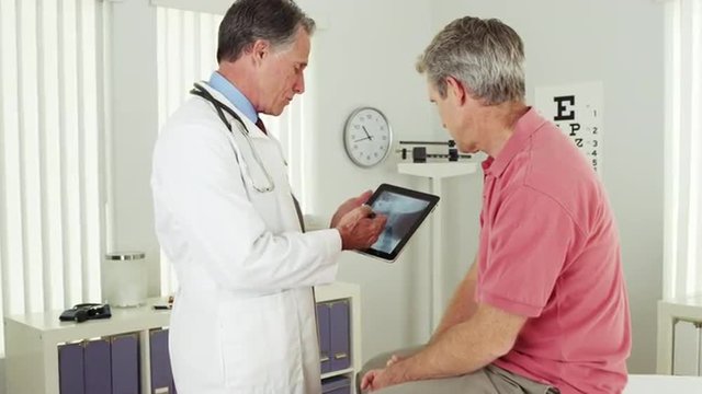 Senior doctor reviewing elderly patient's xray on tablet