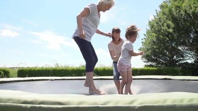 Grandmother, Granddaughter And Mother Bouncing On Trampoline