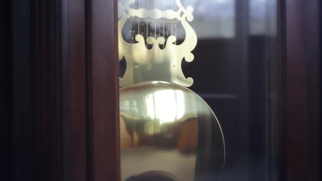An old wooden grandfather clock in the living room with a swinging pendulum