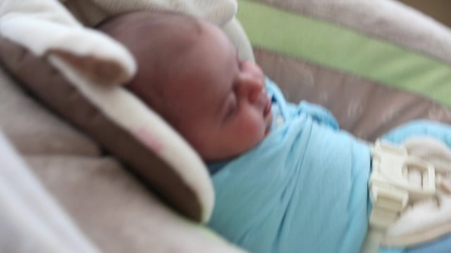 a newborn baby boy in a swing at home