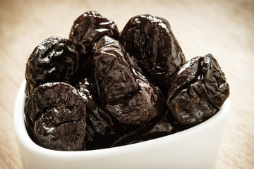 dried plums prunes in white bowl on wooden table