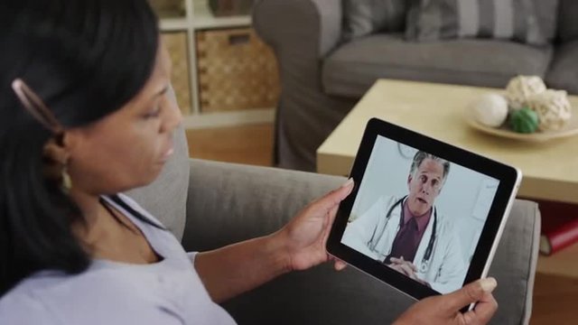 Senior black woman patient listening to doctor talk on tablet