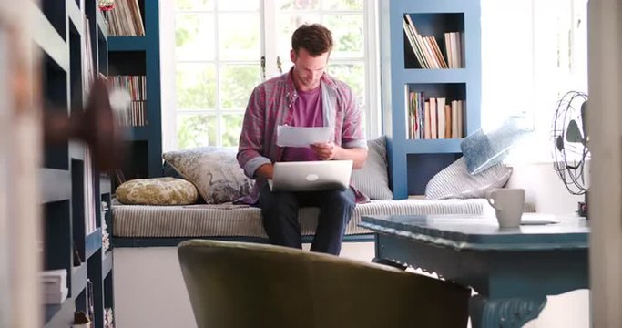 Man Sitting On Couch In Home Office Using Laptop