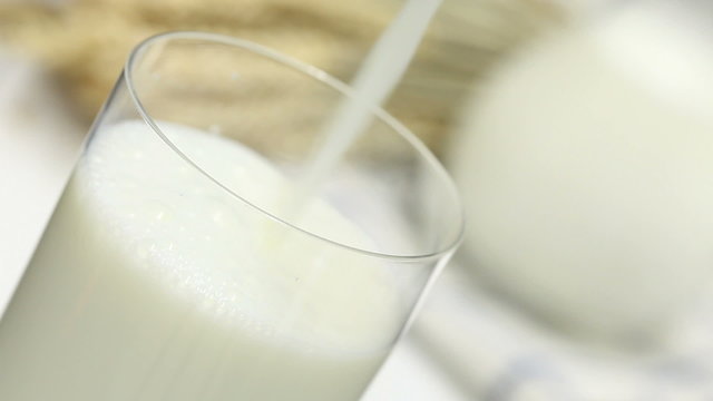Pouring milk into glass on table with agricultural products in the back