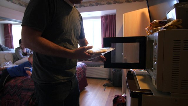 A young family cooks frozen pizza in hotel microwave