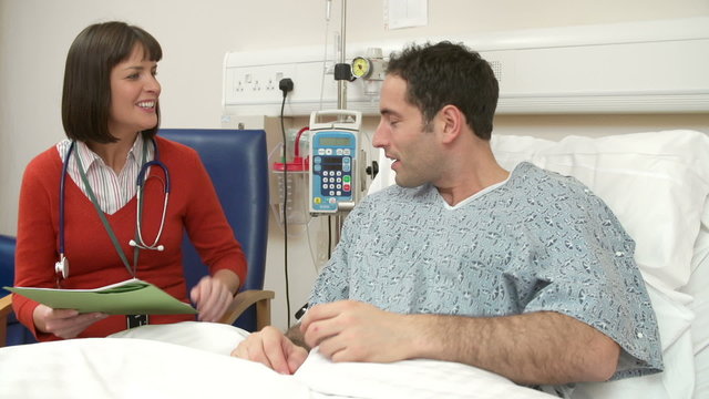 Doctor Sitting At Male Patient's Bedside Having Discussion