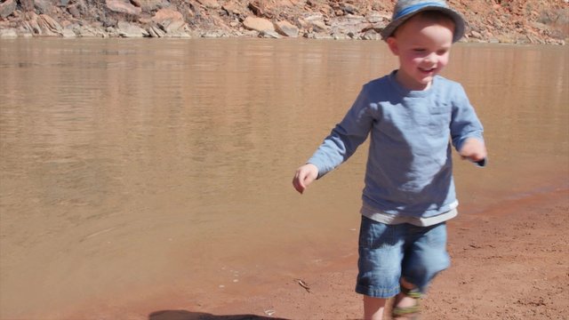 Little boy playing on a sandy beach by river