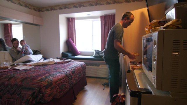 Young family cooks frozen pizza in hotel room microwave