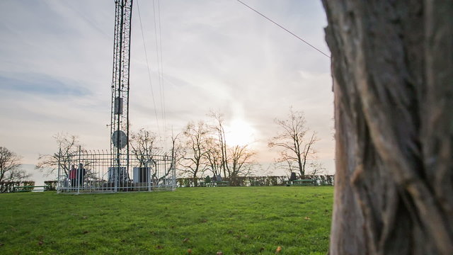 Behind the tree showing park with antenna and sunset