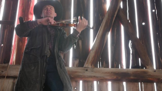 Cowboy plays an old fiddle in barn rafters for the barn dance