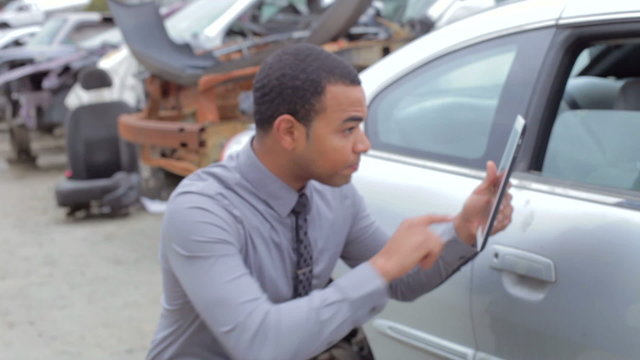 Loss Adjuster Inspecting Car Wreck Using Digital Tablet