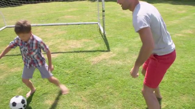 Father And Son Playing Football In Garden At Home
