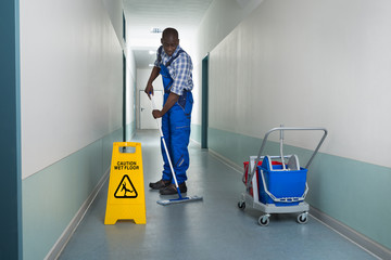 Male Janitor Mopping In Corridor