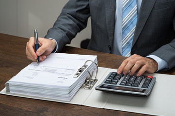 Businessman Calculating Bills In Office