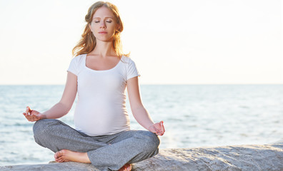 Fototapeta na wymiar Pregnant woman practicing yoga in lotus position on beach at sun