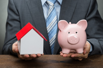 Businessperson With Piggy Bank And House Model