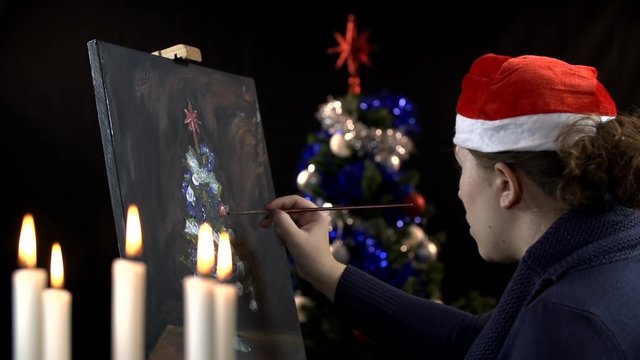 Female artist painting while Christmas tree in background