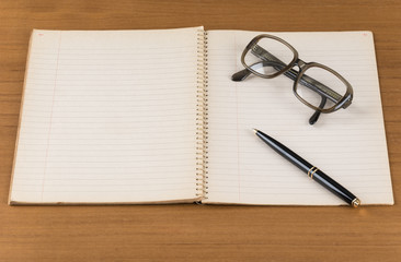 old notebook with pen and glasses on wood table