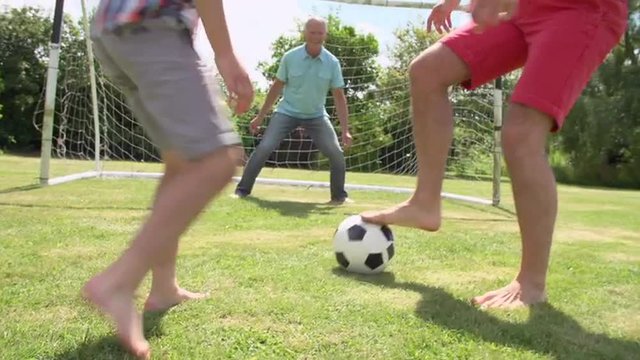 Grandfather, Grandson And Father Playing Football In Garden