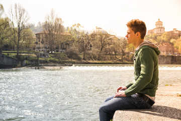 Contemplative teenage boy sitting beside river