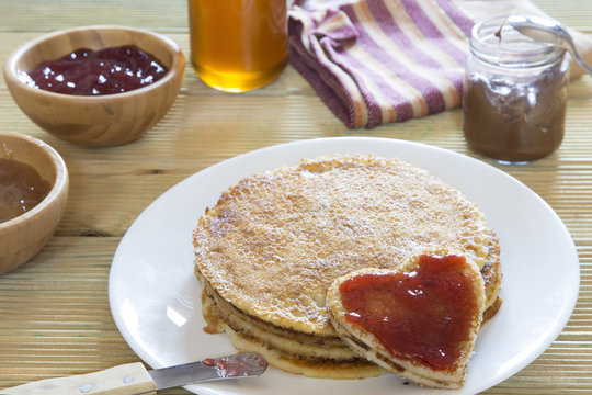 Heart shaped pancake with strawberry jam on stack of pancakes