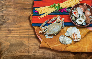 Granchio,frutti di mare  con spaghetti e conchiglie su tessuto etnico e tavola di legno.