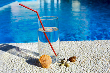 Fresh glass of water drink with seashells,  on border of a swimming pool 