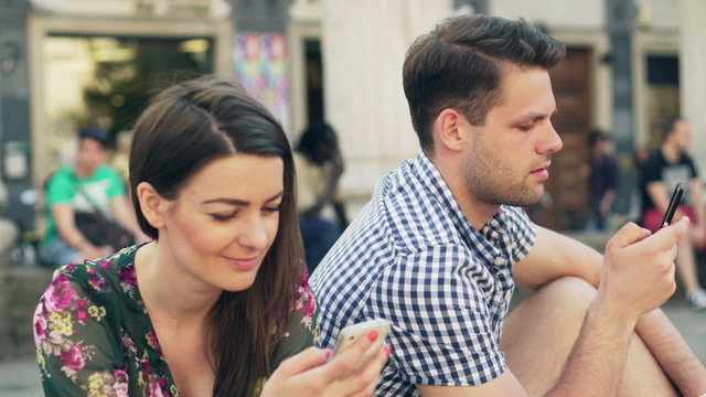 Quiet couple sitting in the city and using smartphones
