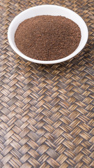 Dried processed tea leaves in white bowl over rustic wicker background