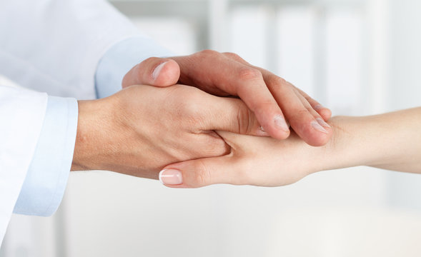 Friendly male doctor's hands holding female patient's hand