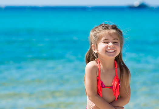 Bambina al mare che ride e gioca, mare turchese come sfondo