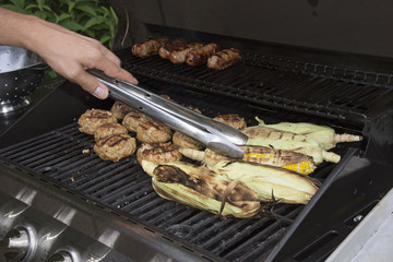 Food cooking on a gas barbecue. Sausages,turkey burgers and corn
