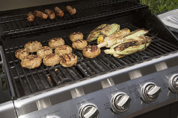 Food cooking on a gas barbecue. Sausages,turkey burgers and corn