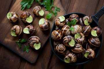 Snails with garlic butter in a frying pan, rustic wooden surface