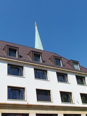 Kirchturmspitze der Altstädter Nicolaikirche vor blauem Himmel im Sonnenschein hinter einem...