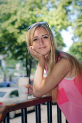 Blonde girl is leaning on the railing and holding a drink