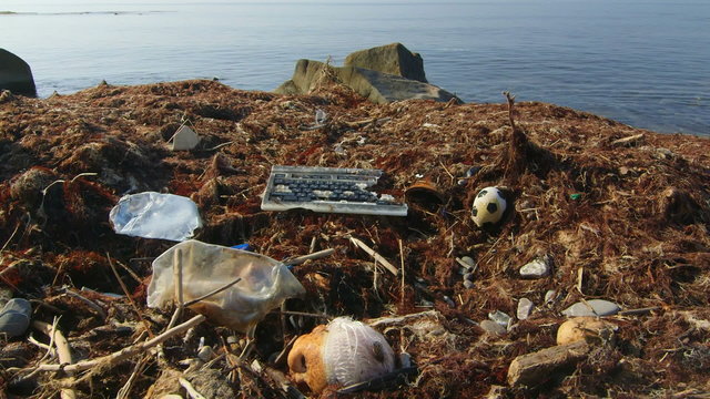 Broken computer keyboard among waste and garbage brought to shore by sea waves