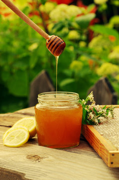 Honey in a glass jar, buckwheat flowers, a lemon and bee honeycombs in a summer sunny day. Honey with flowers and honeycombs